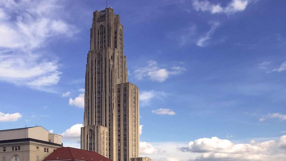 The Cathedral of Learning, an ornate skyscraper reaching into the blue sky, surrounded by clouds, with a red-roofed building partially visible at the bottom. The architecture features vertical lines and a gothic style.
