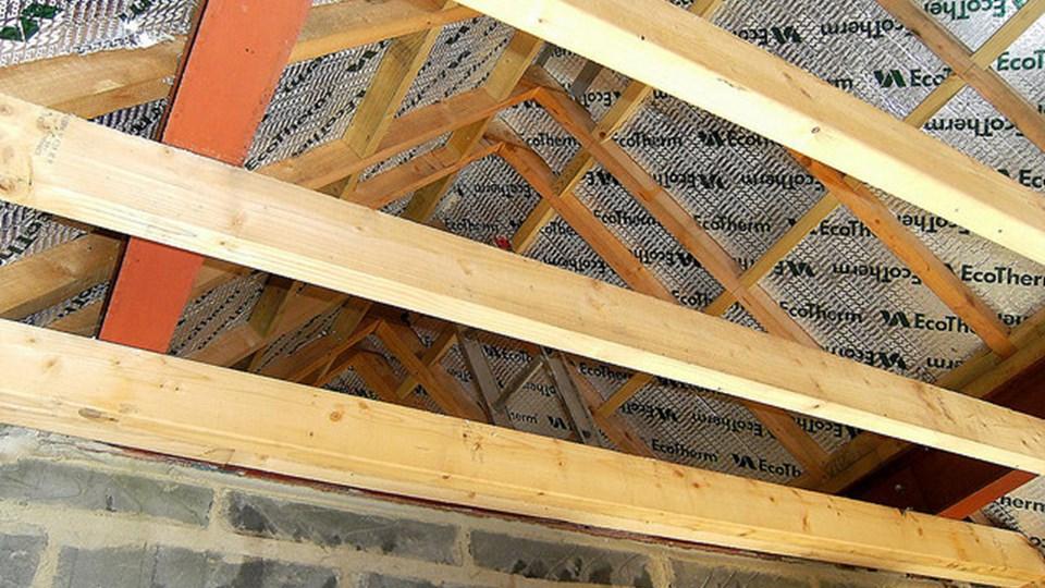 Interior view of a wooden roof structure with exposed beams. Insulation material labeled EcoTherm is visible between the rafters. The ceiling showcases a triangular frame made of wood.