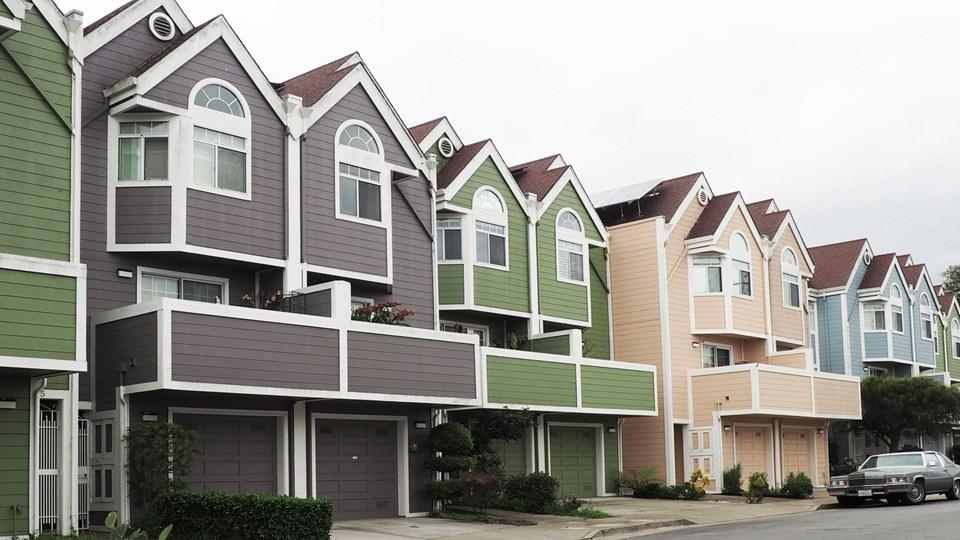 Row of colorful houses with multiple gables, featuring shades of green, purple, and peach. Each house has front balconies and large windows. The scene is set on a cloudy day.